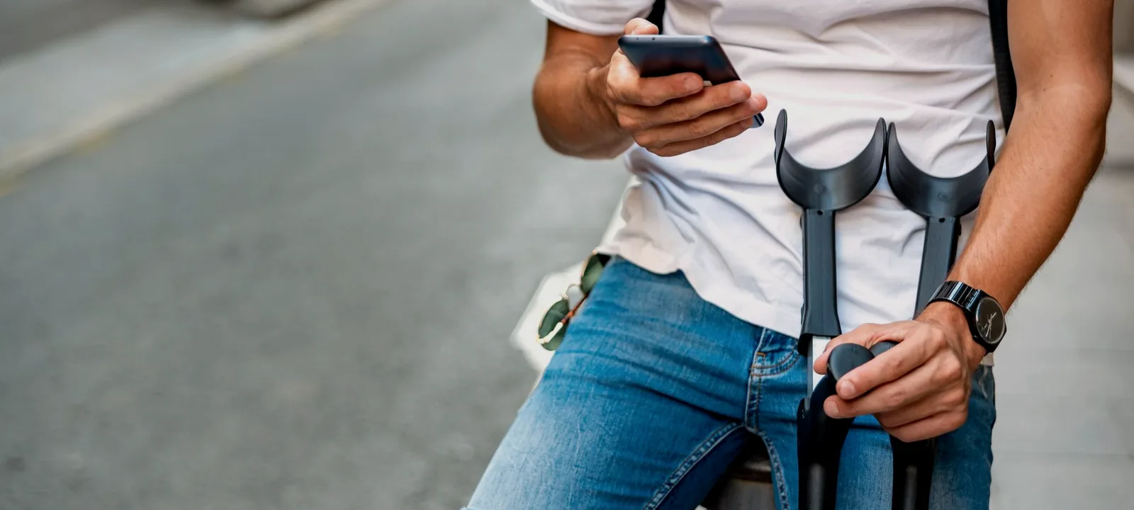 Homem de muletas sentado usando o celular