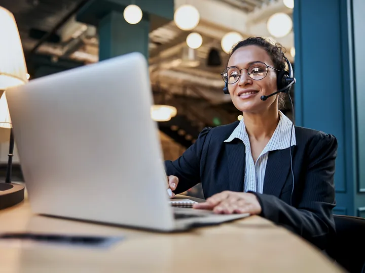 Atendente sorridente com fone de ouvido atende um cliente pelo notebook